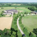 Drone view of full property with pastures in front, equine facility on left, home on right