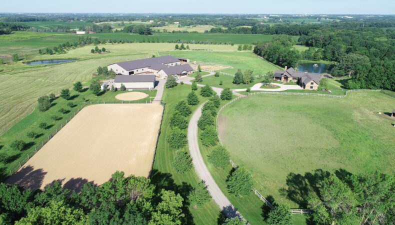 Drone view of full property with pastures in front, equine facility on left, home on right