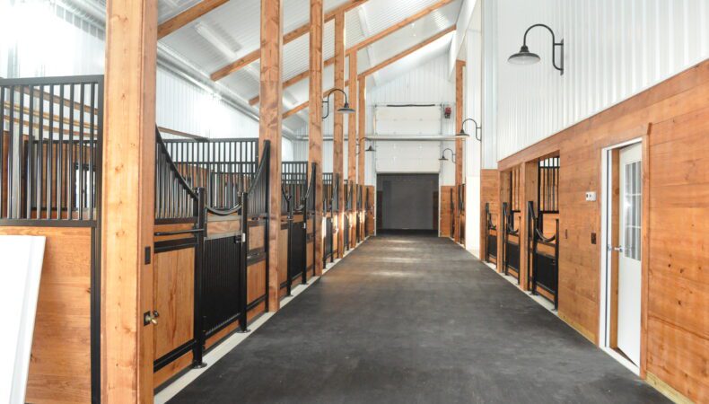 Interior of barn with several horse stalls on left side.