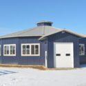 Round riding building with blue siding and white single garage door.
