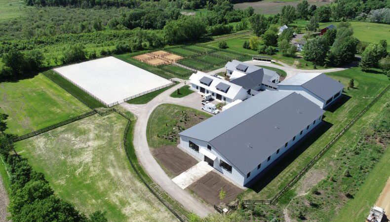 Drone view of property showing large equestrian facility on right.