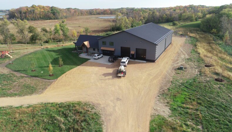 Drone view of large dirt parking area with vehicles parked in front of garage.
