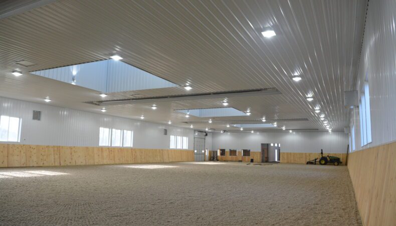 Indoor riding space with bright windows and garage door.