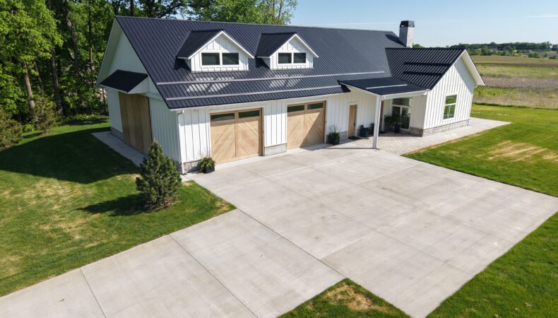 Front view of home with white siding, gray roofing, and wood garage doors.