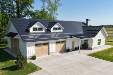 Exterior of home with white siding, gray roofing, and wood garage doors.