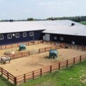 Fenced area on left side of equestrian building showing entrance to the right and barn area on left.