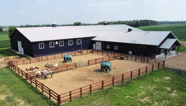 Fenced area on left side of equestrian building showing entrance to the right and barn area on left.
