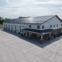 View of full building with entrance on right, garage space on left, parking lot in foreground