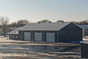 Exterior of large building with 3 large white garage doors in winter.