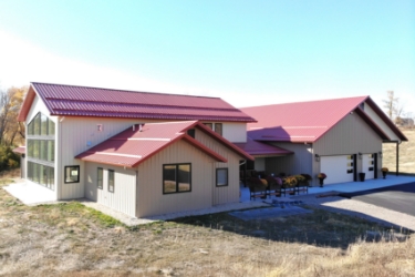 Front of post-frame home with beige siding and red roof.